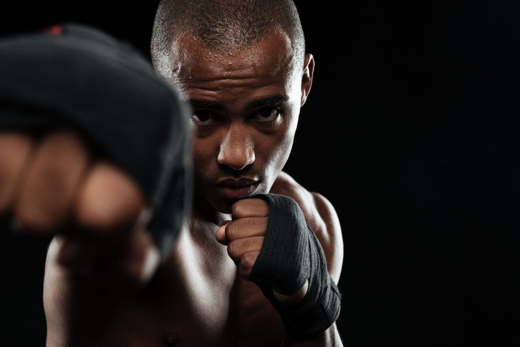 Close-up photo of afroamerican boxer, showing his fists, over black background