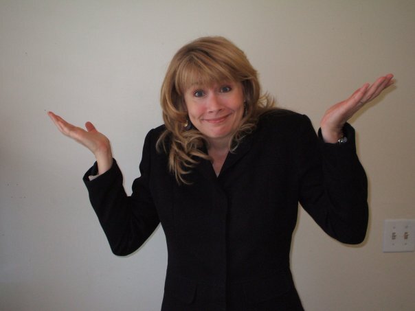 Person with blonde hair wearing a black blazer, raising both hands in a confused or questioning gesture