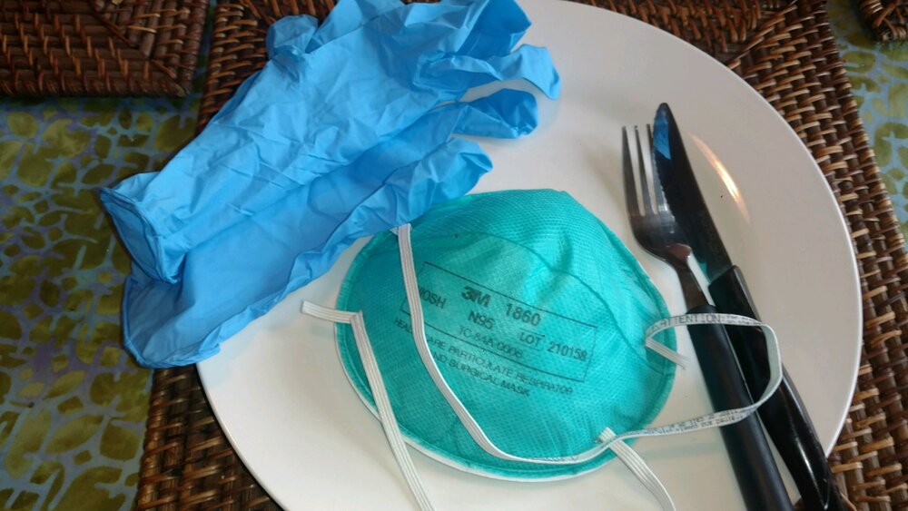 Blue gloves, an N95 mask, and cutlery on a white plate
