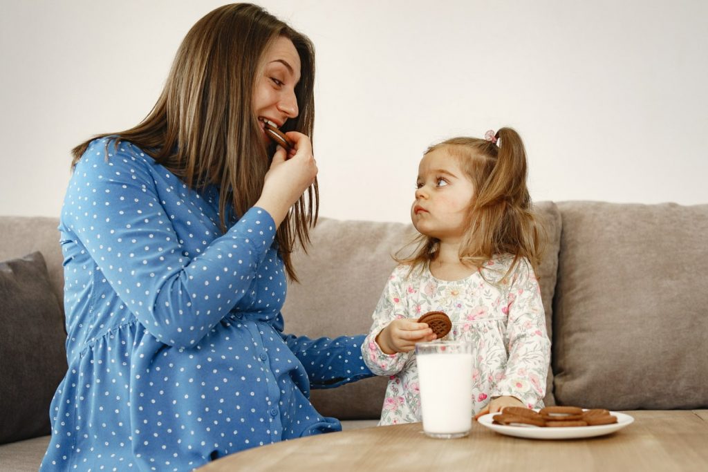 a mom teaching her daughter how to eat cookie