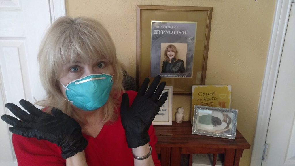 A woman wearing black gloves poses in front of a shelf displaying framed photos and a journal cover on hypnotism