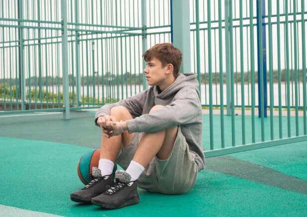 Teenage boy basketball player sitting alone at sportground