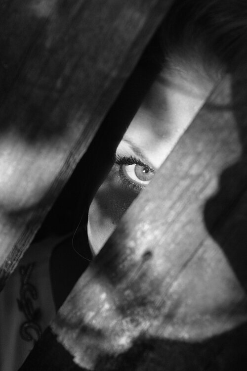 A woman's eye peeks through a narrow gap in wooden planks