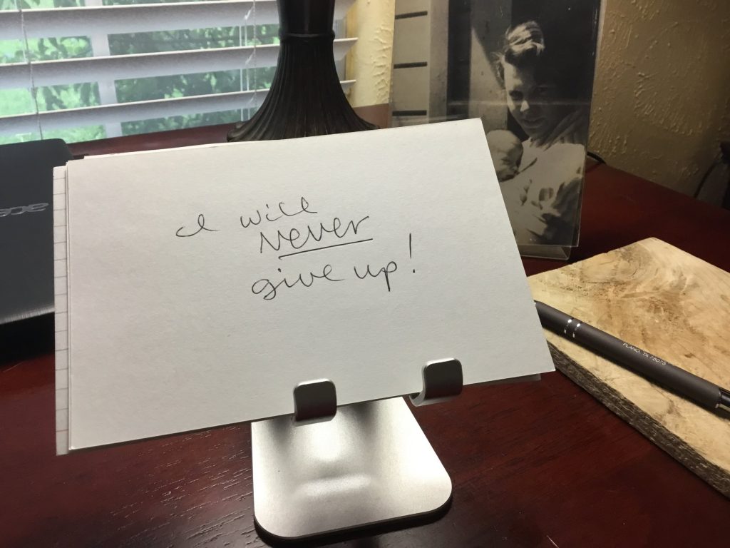 Handwritten note on a desk reads "I will never give up!