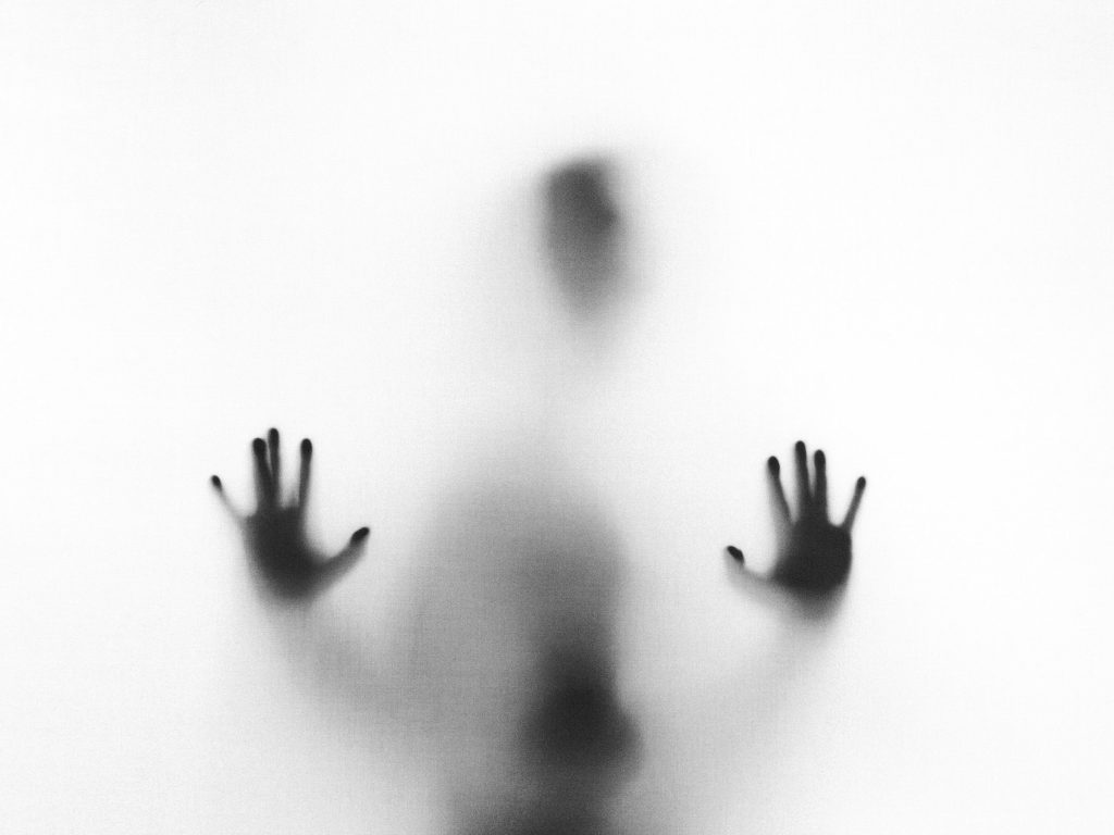 Silhouette of a person pressing their hands against a frosted glass