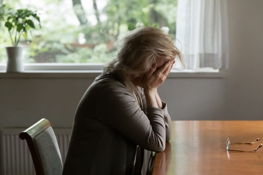 Unhappy old Caucasian woman sit at table at home cry feeling depressed sad suffer from life or health problems. Upset lonely mature female distressed with loneliness solitude, mourn yearn at home.